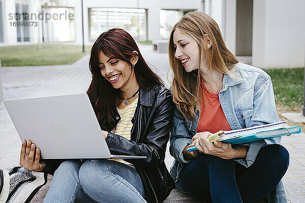 Junge Studentinnen lächelnd bei der Benutzung eines Laptops auf dem Campus