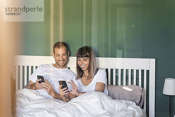 Mittleres erwachsenes Paar lächelt bei der Benutzung eines Mobiltelefons zu Hause