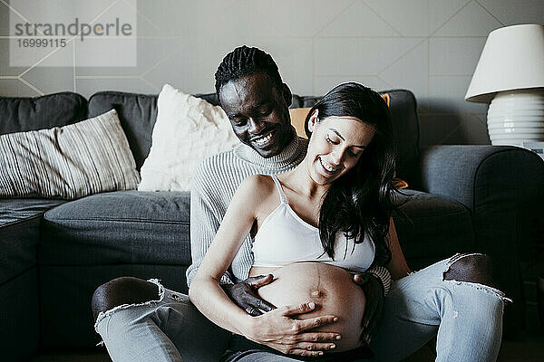 Junger Mann mit schwangerer Frau  die zu Hause ihren Unterleib betrachtet