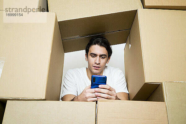 Mann benutzt Mobiltelefon  während er sich auf Kartons stützt