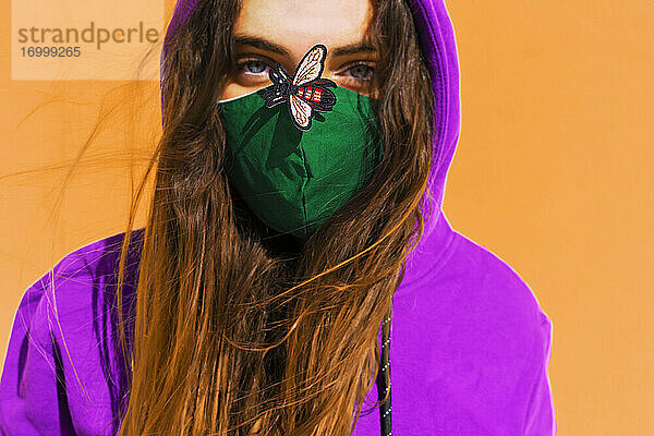 Teenager-Mädchen mit Kapuzenpulli und Gesichtsschutzmaske mit Fliegenaufkleber auf der Nase