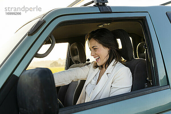 Fröhliche junge Frau am Steuer eines Autos während einer Autoreise