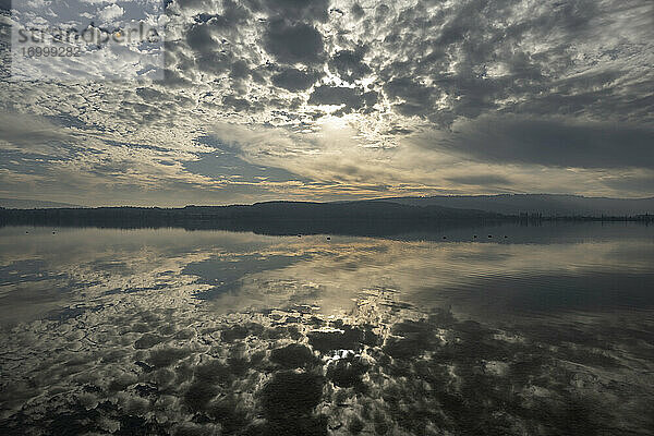 Graue Wolken spiegeln sich im Bodensee in der Abenddämmerung