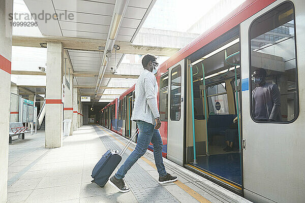 Männlicher Unternehmer auf Geschäftsreise beim Einsteigen in einen U-Bahn-Zug am Bahnhof während einer Pandemie