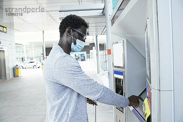 Älterer männlicher Berufstätiger  der während des Coronavirus einen Fahrkartenautomaten am Bahnhof benutzt