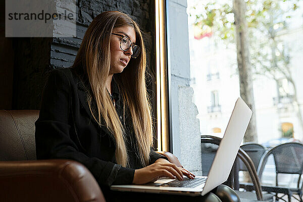Junge Frau mit Brille  die einen Laptop benutzt  während sie in einem Café sitzt