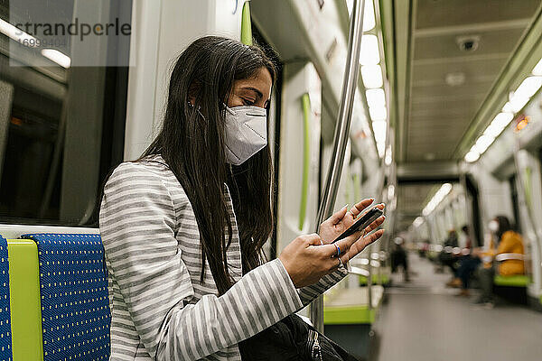 Weiblicher Fahrgast  der in einem U-Bahn-Zug eine Textnachricht über sein Smartphone verschickt