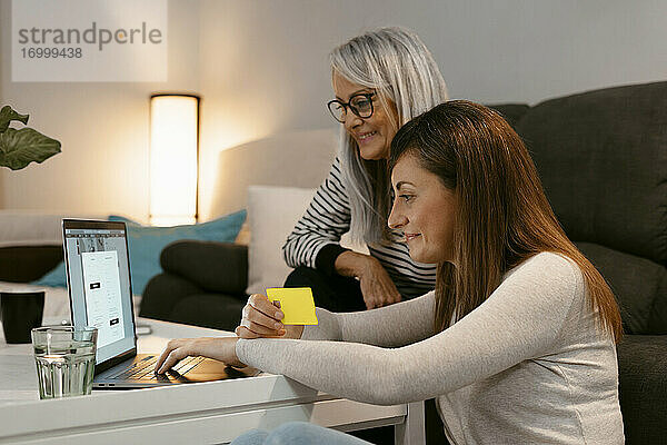 Lächelnde Mutter und Tochter beim Online-Shopping am Laptop  während sie zu Hause sitzen