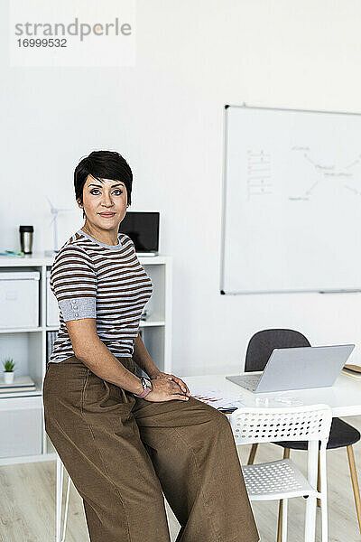 Porträt einer Geschäftsfrau  die am Rand eines Bürotisches sitzt
