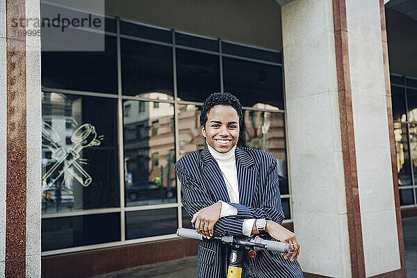 Lächelnde Geschäftsfrau mit Elektro-Scooter in der Stadt