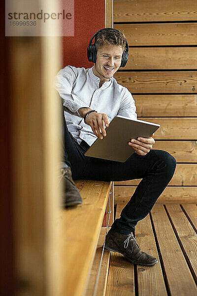 Lächelnder Mann mit Kopfhörern  der ein digitales Tablet benutzt  während er zu Hause sitzt