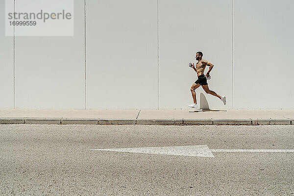 Männlicher Athlet mit nacktem Oberkörper  der auf dem Bürgersteig läuft  mit Pfeilzeichen auf der Straße