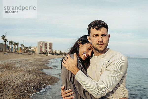 Lächelndes junges Paar umarmt sich am Strand
