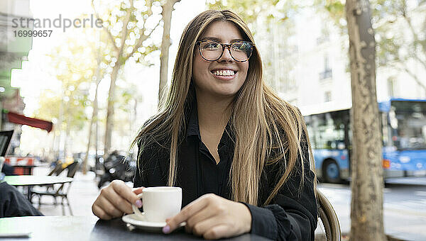 Junge Frau mit Kaffeetasse  die lächelnd in einem Straßencafé in der Stadt sitzt