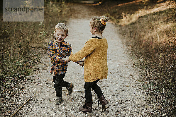 Lächelndes Mädchen und Bruder halten Hände beim Spielen im Wald