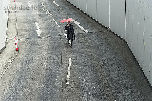 Geschäftsmann mit Regenschirm geht auf Straße mit Pfeil Zeichen
