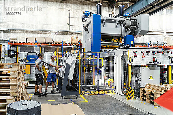 Reife und junge männliche Mitarbeiter testen eine Maschine in einer Fabrik
