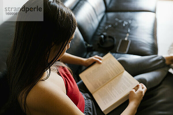 Teenager-Mädchen liest ein Buch  während sie zu Hause auf dem Sofa sitzt