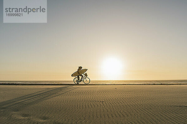 Surfer auf einem Fahrrad während des Sonnenuntergangs am Strand  Costa Nova  Portugal