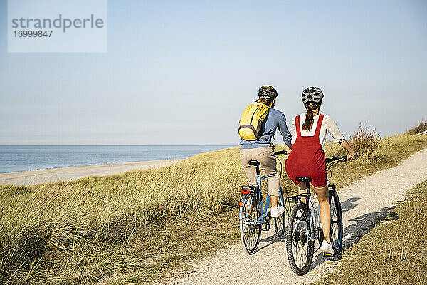 Junges Paar mit Fahrradhelm fährt mit dem Fahrrad gegen den klaren Himmel