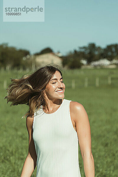 Junge Frau  die sich die Haare wirft  während sie im Park an einem sonnigen Tag steht