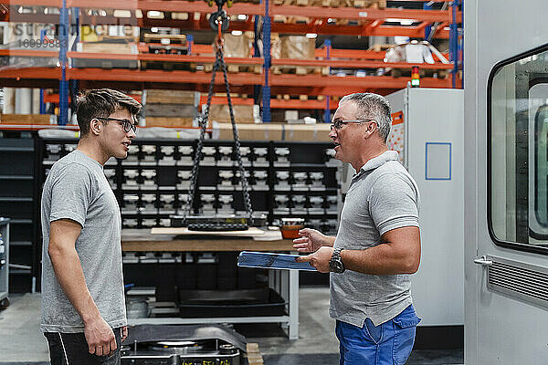 Reifer männlicher Techniker diskutiert mit einem jungen Mitarbeiter in einer Fabrik
