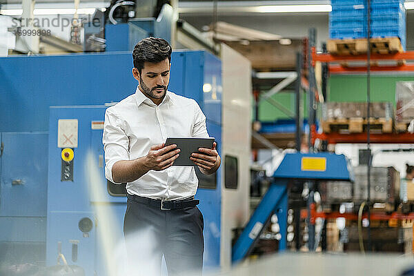 Geschäftsmann  der ein digitales Tablet benutzt  während er in einer Fabrik steht