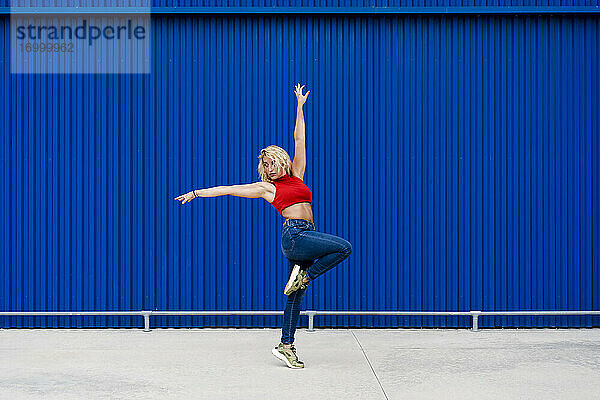 Junge Frau tanzt vor einer blauen Wand in der Stadt