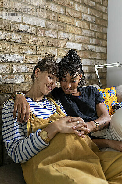 Lesbisches Paar  das zu Hause sitzt und die Hände auf dem Bauch verschränkt