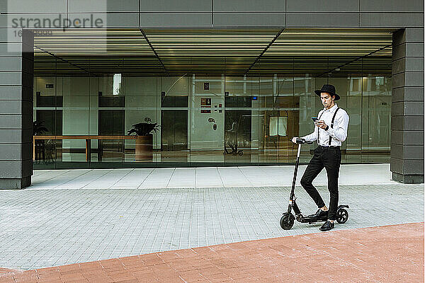 Geschäftsmann auf Elektro-Scooter in der Nähe von modernen Glas-Bürogebäude