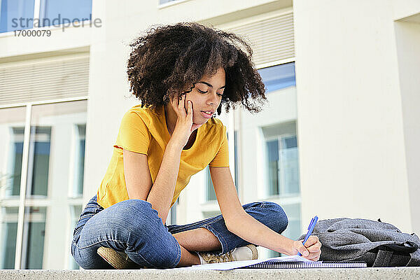 Studentin mit lockigem Haar  die auf dem Universitätscampus sitzt und lernt