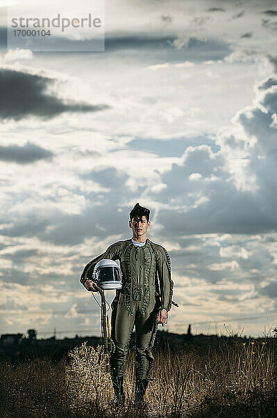 Mann als Astronaut gekleidet auf einer Wiese mit dramatischen Wolken im Hintergrund