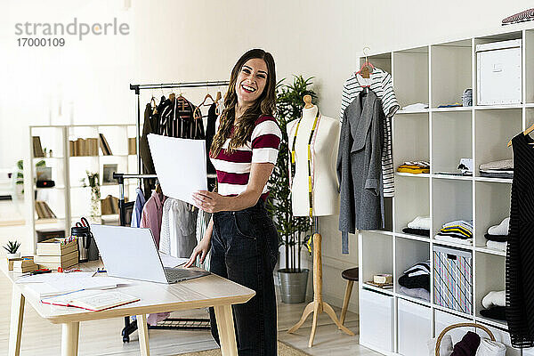 Weibliche Modedesignerin lacht  während sie im Atelier Papier hält