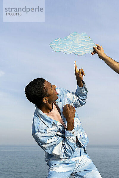 Männchen hält eine ausgeschnittene Wolke auf dem Kopf eines jungen Mannes  der gegen den Himmel steht
