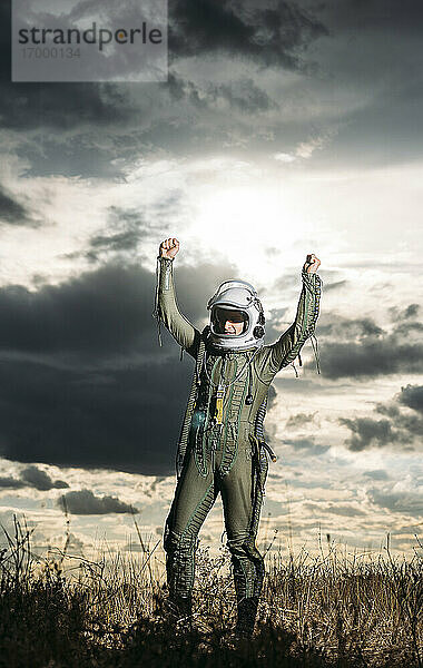 Mann posiert als Astronaut verkleidet auf einer Wiese mit dramatischen Wolken im Hintergrund