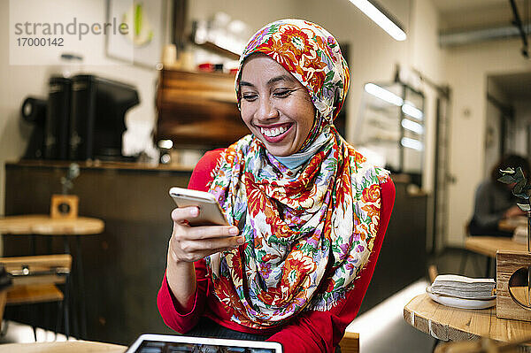 Mittlere erwachsene Frau im Hidschab lächelt  während sie auf ihr Handy schaut