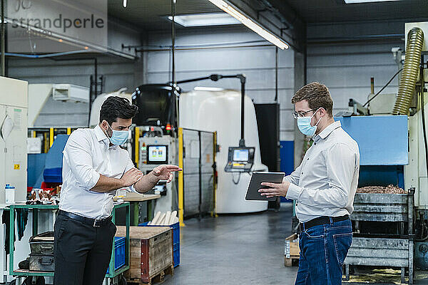 Männliche Mitarbeiter nutzen ein digitales Tablet  während sie in der Fabrik soziale Distanz wahren