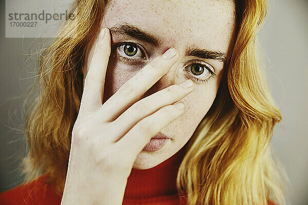Blondes Teenager-Mädchen bedeckt Gesicht mit Hand
