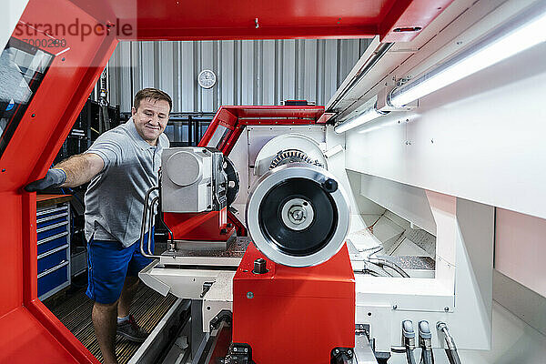 Lächelnder männlicher Arbeiter an einer Maschine in der Industrie