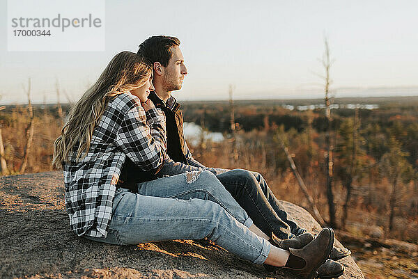 Junges Paar sitzt bei einer Herbstwanderung auf einem Felsen zusammen