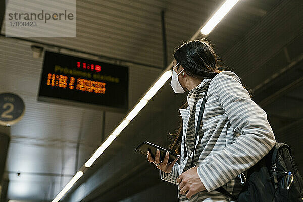 Frau schaut weg  während sie mit ihrem Smartphone am Bahnhof wartet