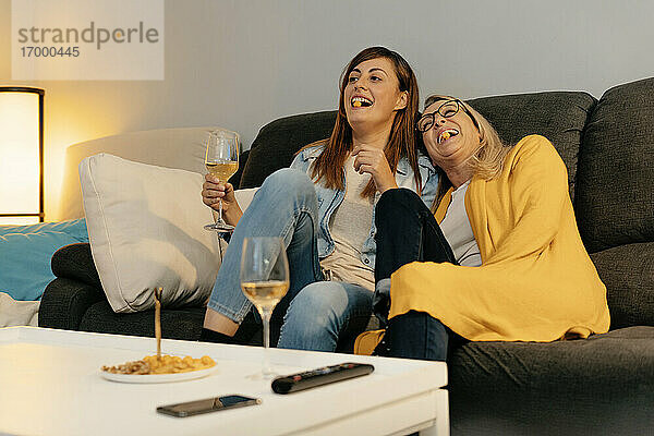 Mutter und Tochter lachen beim Essen von Snacks im Wohnzimmer zu Hause