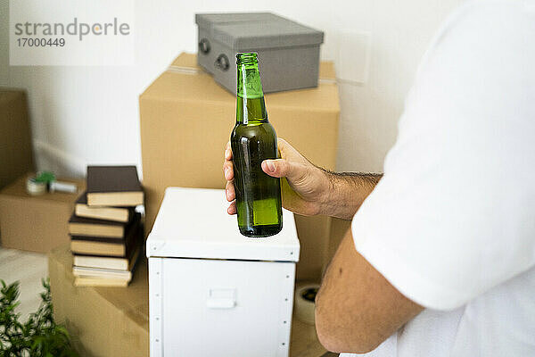 Mann hält Bierflasche in der Hand  während er eine Pause vom Umzug in eine neue Wohnung macht