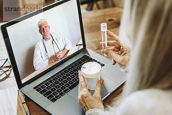 Ältere Frau zeigt dem Arzt ein Reagenzglas bei einem Videoanruf zu Hause