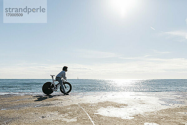 Mittlerer Erwachsener sitzt auf seinem Fahrrad am Strand und beobachtet das Meer