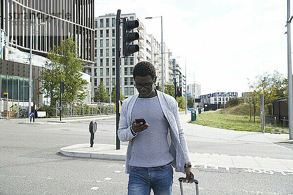Männlicher Unternehmer  der ein Mobiltelefon benutzt  während er in der Stadt auf der Straße geht