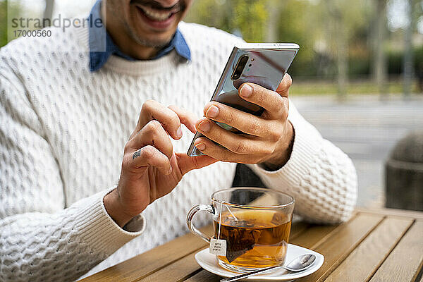 Hände eines Mannes  der in einem Café ein Mobiltelefon benutzt