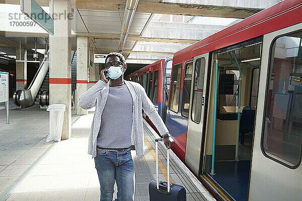 Älterer Geschäftsmann mit Schutzmaske telefoniert auf dem Bahnsteig