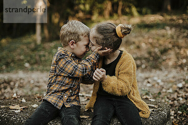 Bruder und Schwester sitzen sich im Herbst im Wald gegenüber