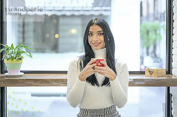 Lächelnde Geschäftsfrau  die eine Tasse Kaffee gegen das Fenster eines Cafés hält